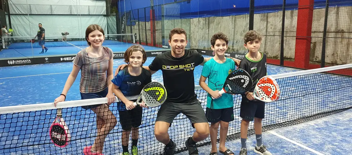 Turma infantil com o professor na quadra, segurando as raquetes